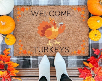 May include: Welcome Turkeys doormat with a brown, orange, and yellow turkey holding a glass of wine. The doormat is made of coir and has a checkered background.