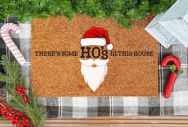 May include: A brown coir doormat with the text "There's some HO'S in this house" and a cartoon image of Santa Claus's face with a red hat and white beard.