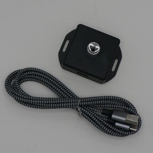 Peut inclure: Un appareil carré noir avec un centre argenté et un câble tressé noir et blanc avec des connecteurs USB et USB-C. L'appareil a un design en forme de cœur au centre.