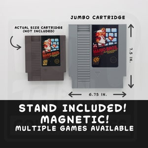 May include: A gray jumbo cartridge with the Super Mario Bros. logo, measuring 7.5 inches tall and 6.75 inches wide. The image also shows an actual size cartridge (not included). The text "STAND INCLUDED! MAGNETIC! MULTIPLE GAMES AVAILABLE" is displayed.