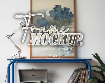 May include: A framed artwork with a landscape scene featuring blue trees and a full moon. The frame is brown, and the artwork is displayed on a blue shelf with a record player and records. The text "Frame Mockup" is overlaid on the image.