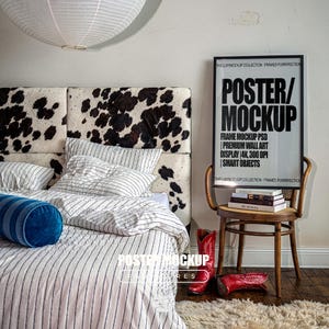 May include: A bedroom scene featuring a cow print headboard, white and blue striped bedding, and a blue bolster pillow. A framed poster with the text POSTER/MOCKUP sits on a wooden chair next to a stack of books and red cowboy boots.