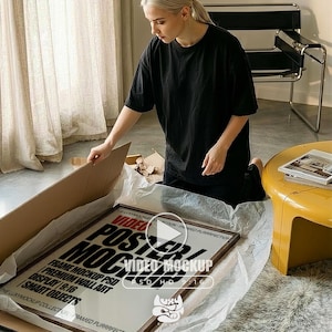 May include: A framed poster mockup with the text "VIDEO POSTER MOCKUP" in a brown frame. The poster includes text such as "FRAME MOCKUP PSD" and "PREMIUM WALL ART". The image shows a person opening the package.