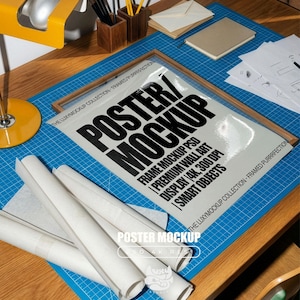 May include: A poster mockup with the text "POSTER / MOCKUP" in large black letters. The poster is in a wooden frame and rests on a blue grid surface. Rolled-up white paper and stationery are also visible.