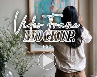 May include: A large rectangular wooden picture frame containing an abstract painting with blue, yellow, and pink shapes. The text "Video Frame MOCKUP. PSD" is overlaid in white script and block lettering. A clear glass vase with white flowers sits nearby.