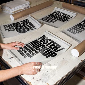 May include: A mockup of posters with the text "POSTER/MOCKUP" in bold black letters. The posters are on a light-colored surface, with rolled-up poster tubes and a stack of papers nearby. The text includes "FRAME MOCKUP PSD, DISPLAY 4K, 300 DPI, PREMIUM WALL ART, SMART OBJECTS."