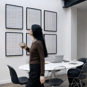6 A-size frames gallery wall video mockup PSD. A woman hangs black poster mockups in a modern dining room. Premium wall art display for social media.