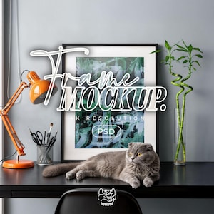 May include: A black framed art print mockup with the text "Frame Mockup" in a white, stylized font. An orange desk lamp, a gray cat, and a vase of bamboo are on the black desk. The image is a 4K resolution PSD.