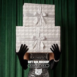 以下が含まれることがあります： グレーと白のストライプとリボンが付いた模様の紙で包まれた2つの長方形のギフトボックス。黒い手袋とスパンコールのドレスを着た人が箱を持っています。画像には「GIFT BOX MOCKUP」というテキストが含まれています。