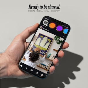 May include: A smartphone displays a social media post with the text "Ready to be shared." The post features a painting with the words "Let Grow" and a person adjusting the artwork. The phone's interface includes social media icons.