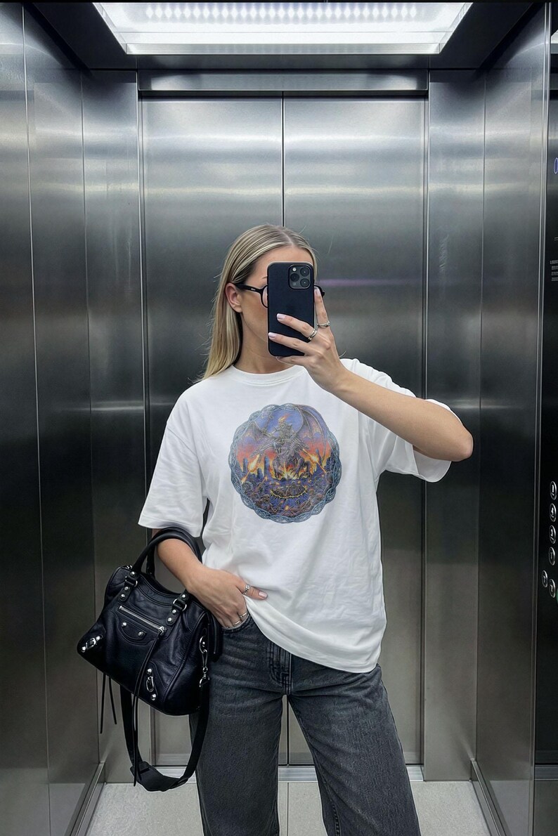 Oversized white t-shirt mockup featuring a trendy woman taking a mirror selfie in an elevator, ideal for streetwear brands. tshirt mock up for e-commerce and social media posts.