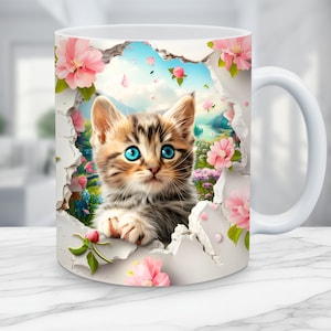 Puede incluir: Taza de cerámica blanca con una imagen colorida de un gatito mirando a través de un trozo de papel rasgado con flores rosas y un cielo azul en el fondo.