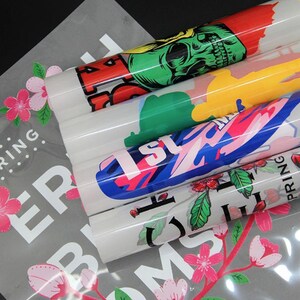 May include: A stack of five iron-on heat transfer vinyl sheets with various colorful designs. The designs include a skull, a graphic with the word "1st", and a floral pattern. The sheets are packaged in a clear plastic bag with a white background and the words "Spring Blooms" printed on it.