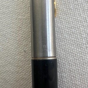 May include: A close-up of a silver and black pen with a gold-colored clip. The pen has the text "MADE IN U.S.A." printed on the barrel. The pen is a writing instrument.