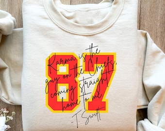 Może przedstawiać: Beżowa bluza z czerwono-żółtym nadrukiem graficznym, na którym widnieje napis "Karma is the guy on the Chiefs, coming straight home to me - T. Swift".