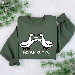 May include: A green sweatshirt with a white graphic of two geese bumping into each other. The text "Goose Bumps" is printed below the geese.