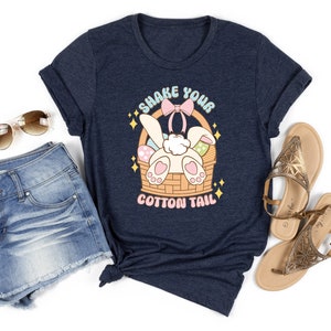 K&ouml;nnte beinhalten: Ein marineblaues T-Shirt mit einem Aufdruck eines Kaninchens in einem Korb mit Eiern. Der Text auf dem Shirt lautet "Shake Your Cotton Tail".