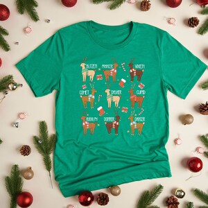 May include: A green t-shirt featuring a festive reindeer design. Each reindeer is labeled with a name like "Blitzen" and "Comet". The shirt is surrounded by Christmas ornaments, pine needles, and candy.