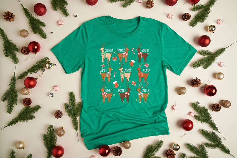 May include: A green t-shirt featuring a festive reindeer design. Each reindeer is labeled with a name like "Blitzen" and "Comet". The shirt is surrounded by Christmas ornaments, pine needles, and candy.