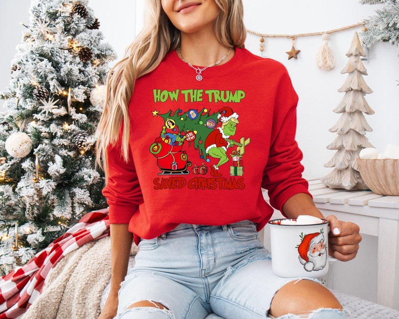 以下が含まれることがあります： 緑色のグリンチのキャラクターと「How the Trump Saved Christmas」というテキストが書かれた赤いクリスマスセーター。