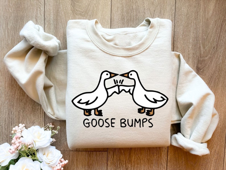 May include: A light beige sweatshirt with a graphic of two cartoon geese facing each other with the text "GOOSE BUMPS" printed below.