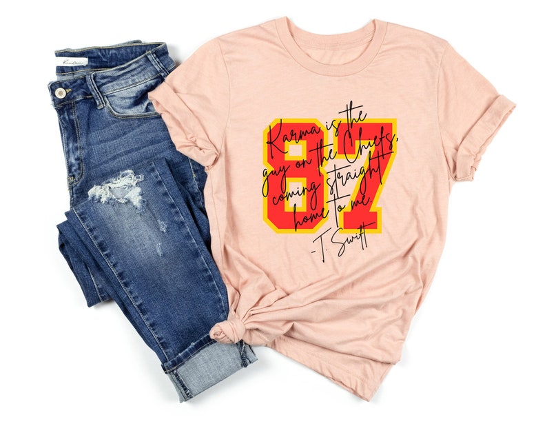 Może przedstawiać: R&oacute;żowy t-shirt z czerwono-ż&oacute;łtym nadrukiem, na kt&oacute;rym widnieje napis "Karma is the guy on the Chiefs, coming straight home to me - T. Swift".
