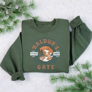 Op de afbeelding: Een groen sweatshirt met een vintage-stijl afbeelding van een berglandschap en de tekst "The Forgotten Realms of Baldur's Gate: Sword Coast".