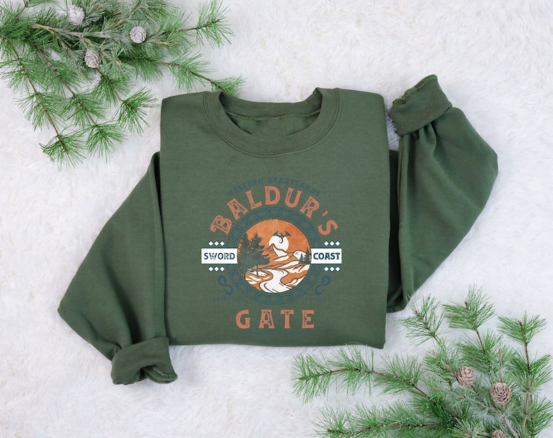 Op de afbeelding: Een groen sweatshirt met een vintage-stijl afbeelding van een berglandschap en de tekst "The Forgotten Realms of Baldur's Gate: Sword Coast".