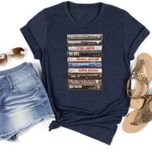 May include: A navy blue t-shirt with a graphic of a stack of vintage cassette tapes featuring the names of popular artists like Madonna, Cyndi Lauper, and Van Halen.