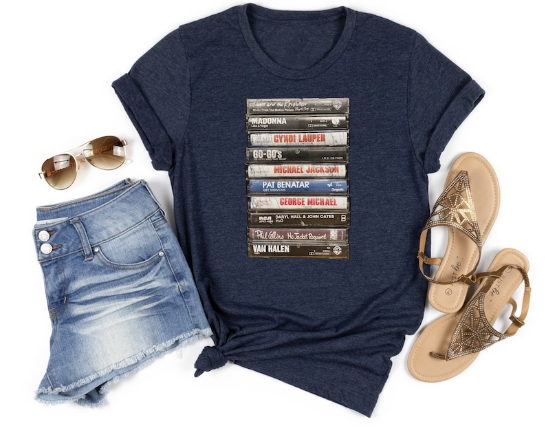 May include: A navy blue t-shirt with a graphic of a stack of vintage cassette tapes featuring the names of popular artists like Madonna, Cyndi Lauper, and Van Halen.