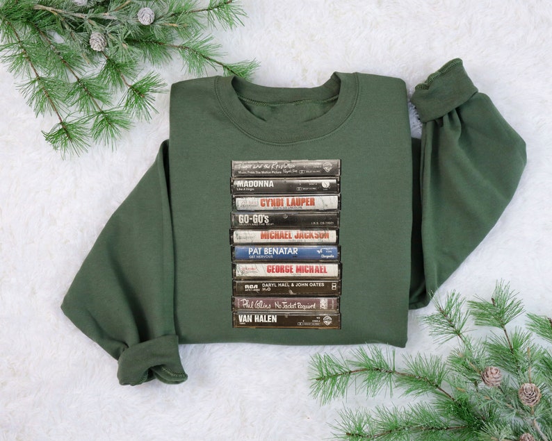 May include: A dark green sweatshirt with a stack of vintage cassette tapes printed on the front. The tapes feature artists such as Madonna, Cyndi Lauper, and Van Halen.
