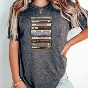 May include: A gray t-shirt with a stack of vintage cassette tapes featuring artists like Madonna, Cyndi Lauper, and Van Halen.