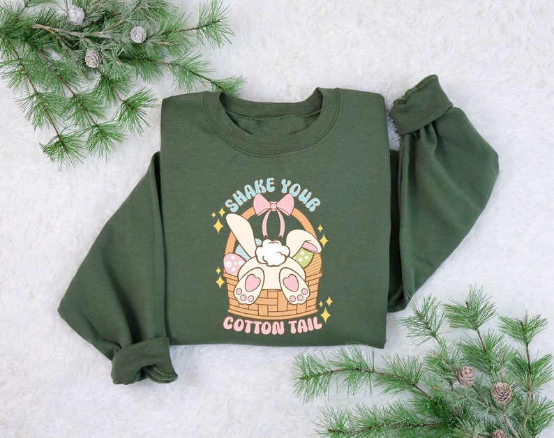 K&ouml;nnte beinhalten: Gr&uuml;nes Sweatshirt mit einem Aufdruck eines Hasen in einem Korb mit dem Text "Shake Your Cotton Tail".