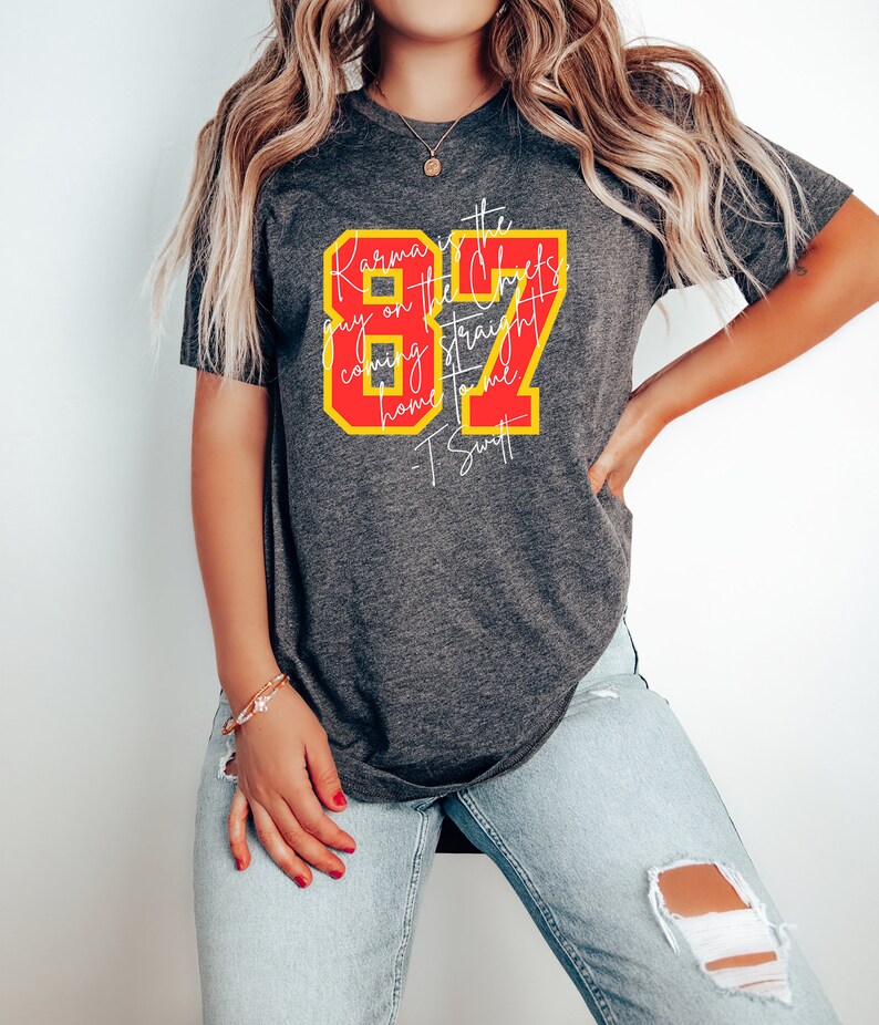 Może przedstawiać: Szary T-shirt z czerwono-ż&oacute;łtym nadrukiem, na kt&oacute;rym widnieje napis "Karma is the guy on the Chiefs coming straight home to me - T. Swift" oraz liczba 87.