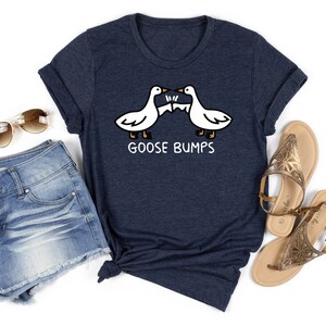 May include: A navy blue t-shirt with a white graphic of two geese bumping heads. The text "GOOSE BUMPS" is printed below the geese.