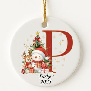 May include: White ceramic Christmas ornament with a red letter "P" and a gold string. The ornament features a snowman, a reindeer, a Christmas tree, and gifts. The name "Parker" and the year "2025" are printed at the bottom.