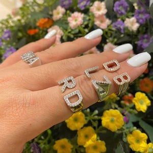 May include: A set of four silver rings with diamond-like accents. Each ring features a different letter, spelling out the word "RD" and "LB".