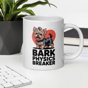 May include: White ceramic mug featuring a cartoon Yorkshire Terrier with a red heart background. The mug has the text "BARK PHYSICS BREAKER" in black and white. The mug is on a white surface.