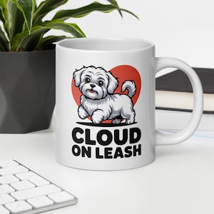 Puede incluir: Taza de cerámica blanca con una ilustración de dibujos animados de un perro blanco y esponjoso y un corazón rojo. La taza tiene el texto "CLOUD ON LEASH" en negro y en negrita.
