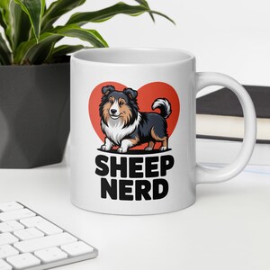 Puede incluir: Taza de cerámica blanca con una ilustración de perro de dibujos animados frente a un corazón rojo. El perro es negro, marrón y blanco. Las palabras "SHEEP NERD" están impresas en letras negras en negrita debajo del perro.