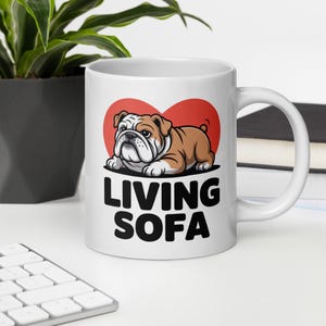 Könnte beinhalten: Weiße Keramiktasse mit einer Cartoon-Bulldoggen-Illustration in Braun und Weiß, vor einem roten Herz. Auf der Tasse steht in fetten schwarzen Buchstaben "LIVING SOFA".