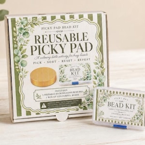 May include: A square cardboard box labelled Reusable Picky Pad Bead Kit with green striped borders and eucalyptus illustrations. The box displays a 10 cm silicone pad and a small clear plastic container filled with colourful beads for crafting.