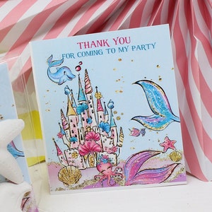 May include: Thank you for coming to my party card with a mermaid tail, a castle, and an octopus on a blue background with gold glitter.
