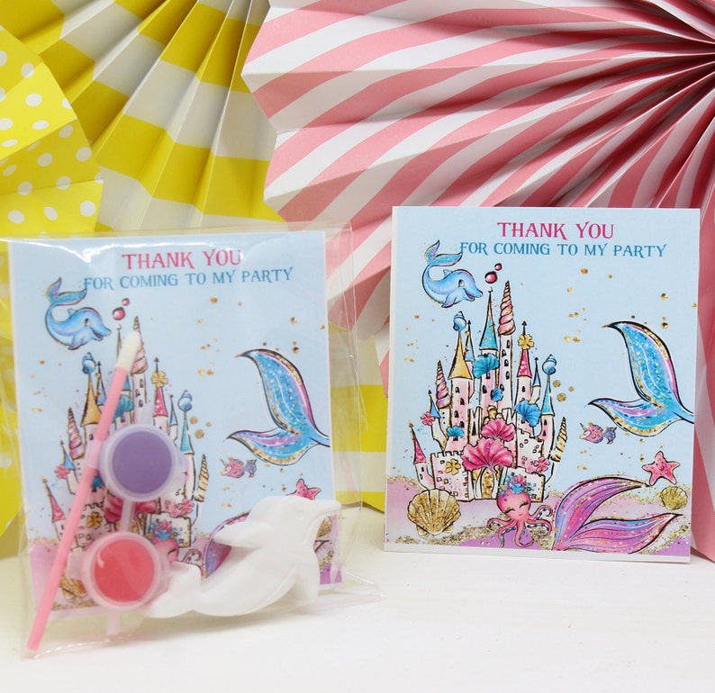 May include: Thank you for coming to my party favor bags with a mermaid castle design, paint, and a brush. The bags are clear plastic and have a white dolphin figurine inside.