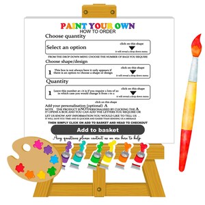 May include: A white easel with a sign that says "Paint Your Own How To Order". The sign has instructions on how to choose a quantity, select an option, choose a shape or design, and add personalization. There is a paint palette with paint tubes and a paintbrush.