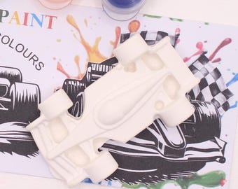 May include: A white race car-shaped craft kit with the words "PAINT COLOURS" visible. The kit includes paint pots in orange and blue, and a checkered flag design. The image has colorful paint splatters.