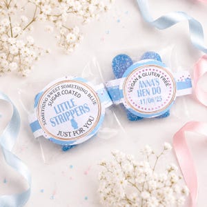 May include: Two clear plastic bags containing blue sugar-coated sweets. Each bag features a circular label with blue and pink text. One label reads "Something Sweet Something Blue Little Strippers Just For You" and the other "Anna's Hen Do 11/06/25 Vegan & Gluten Free".