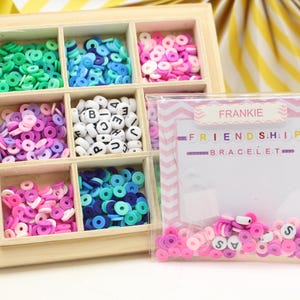 May include: A wooden box with six compartments filled with colourful plastic beads and letter beads. The box is labelled "Frankie Friendship Bracelet".