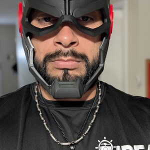 May include: A black and red 3D printed helmet with a skull and tentacles design. The helmet has a visor and a chin guard. The person wearing the helmet is wearing a black shirt with a silver necklace.