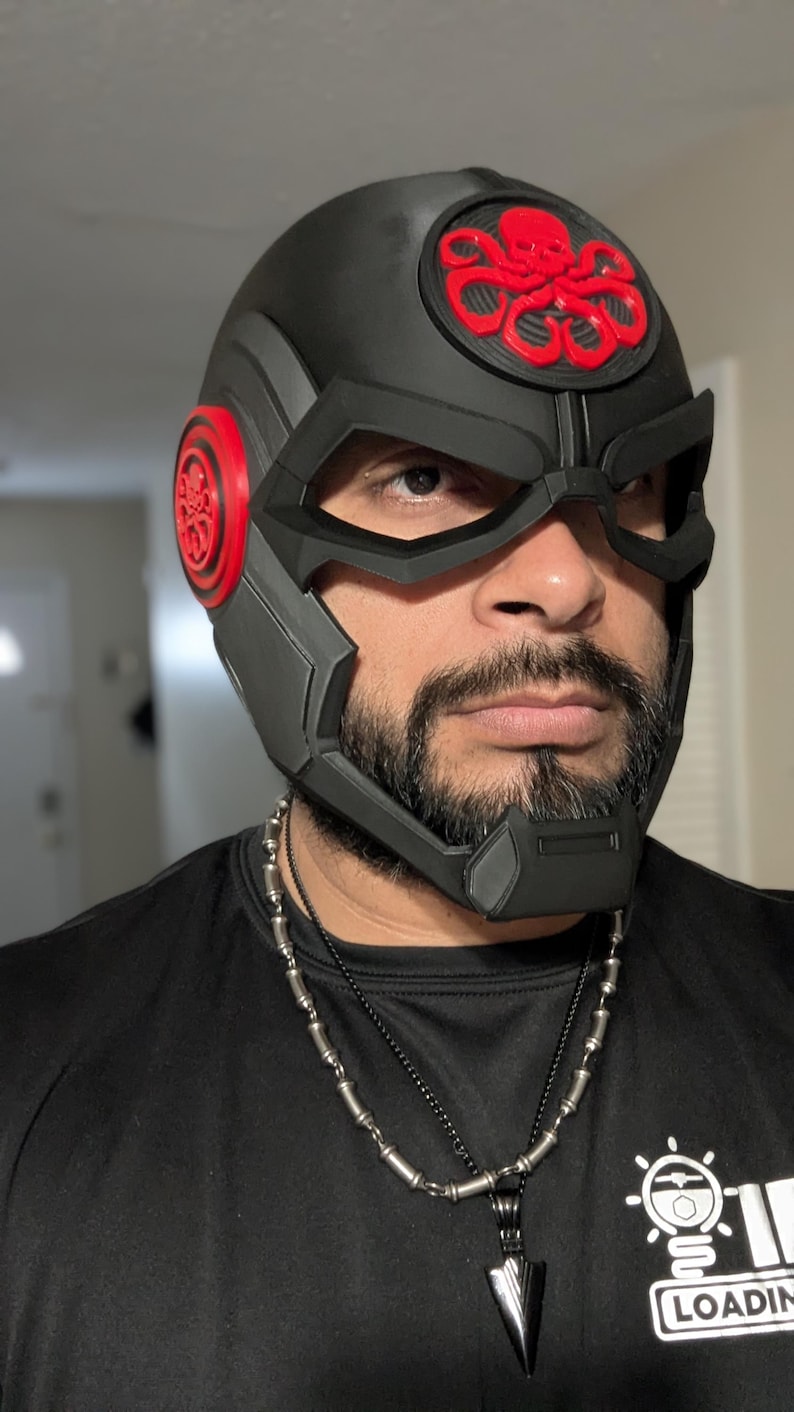 May include: A black helmet with a red Hydra logo on the top. The helmet has a black visor and a black chin strap. The helmet is worn by a person with a beard.